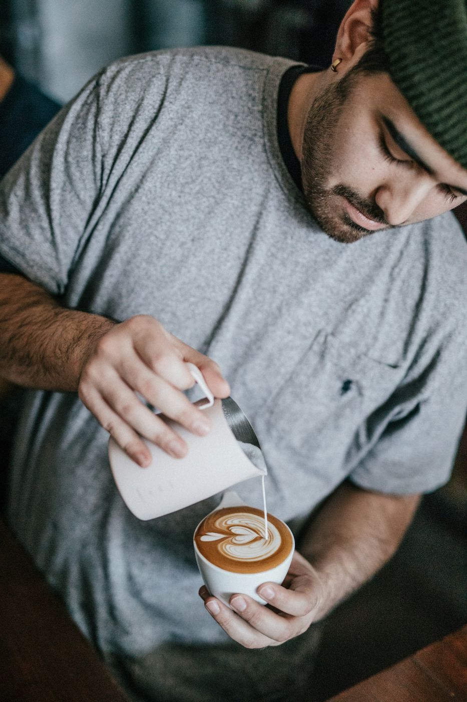 A barista in a knit cap pours latte art into a cappuccino