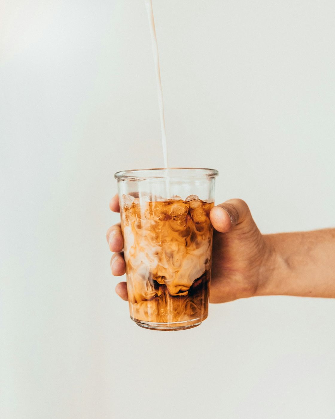 Coffee poured over ice into a clear glass held in a hand